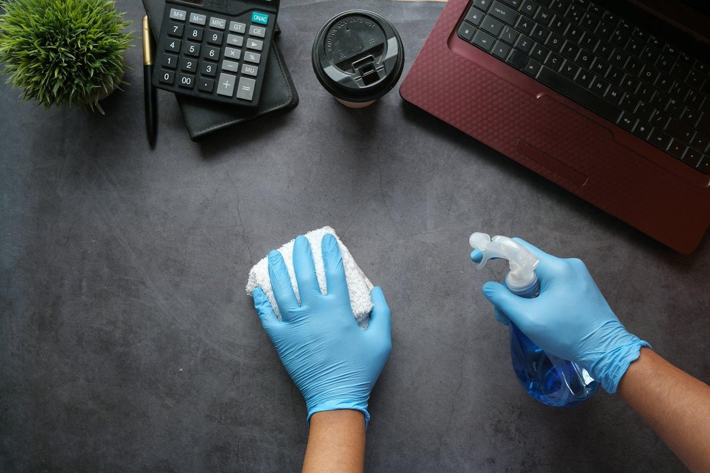 Reinigung eines Schreibtisches mit Handschuhen und Sprühflasche